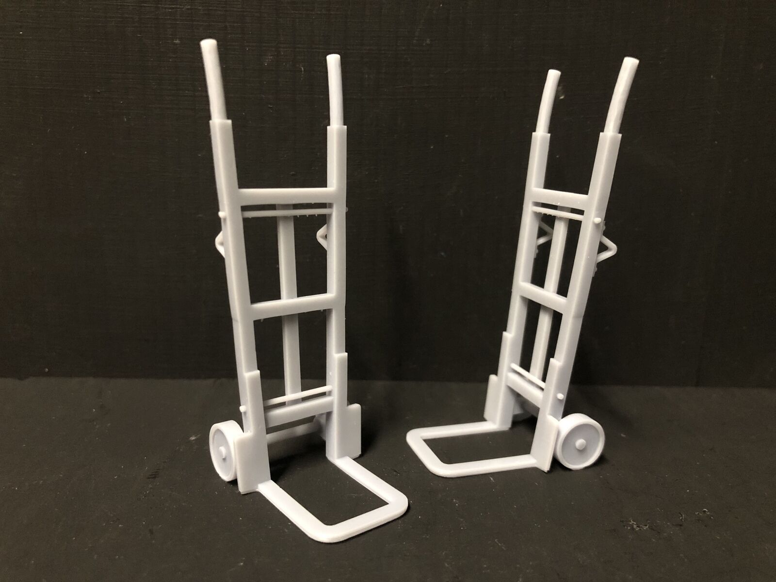 Unpainted 16mm scale resin model sack trolleys, supplied as two grey platform and workshop accessories for model railway layouts