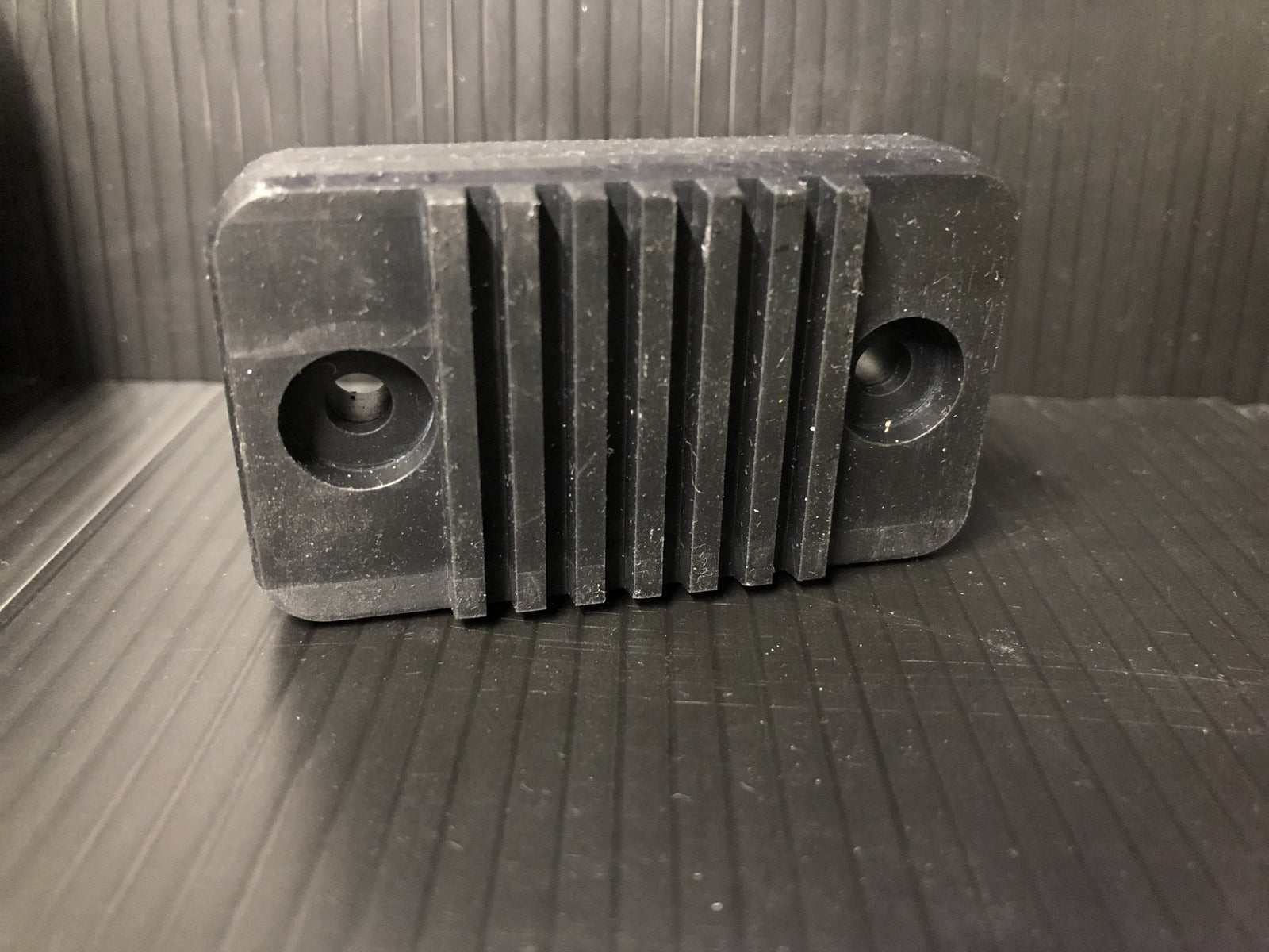 Black covert AirTag case styled as a small electronics box with heatsink fins for discreet tracking on vehicles or equipment