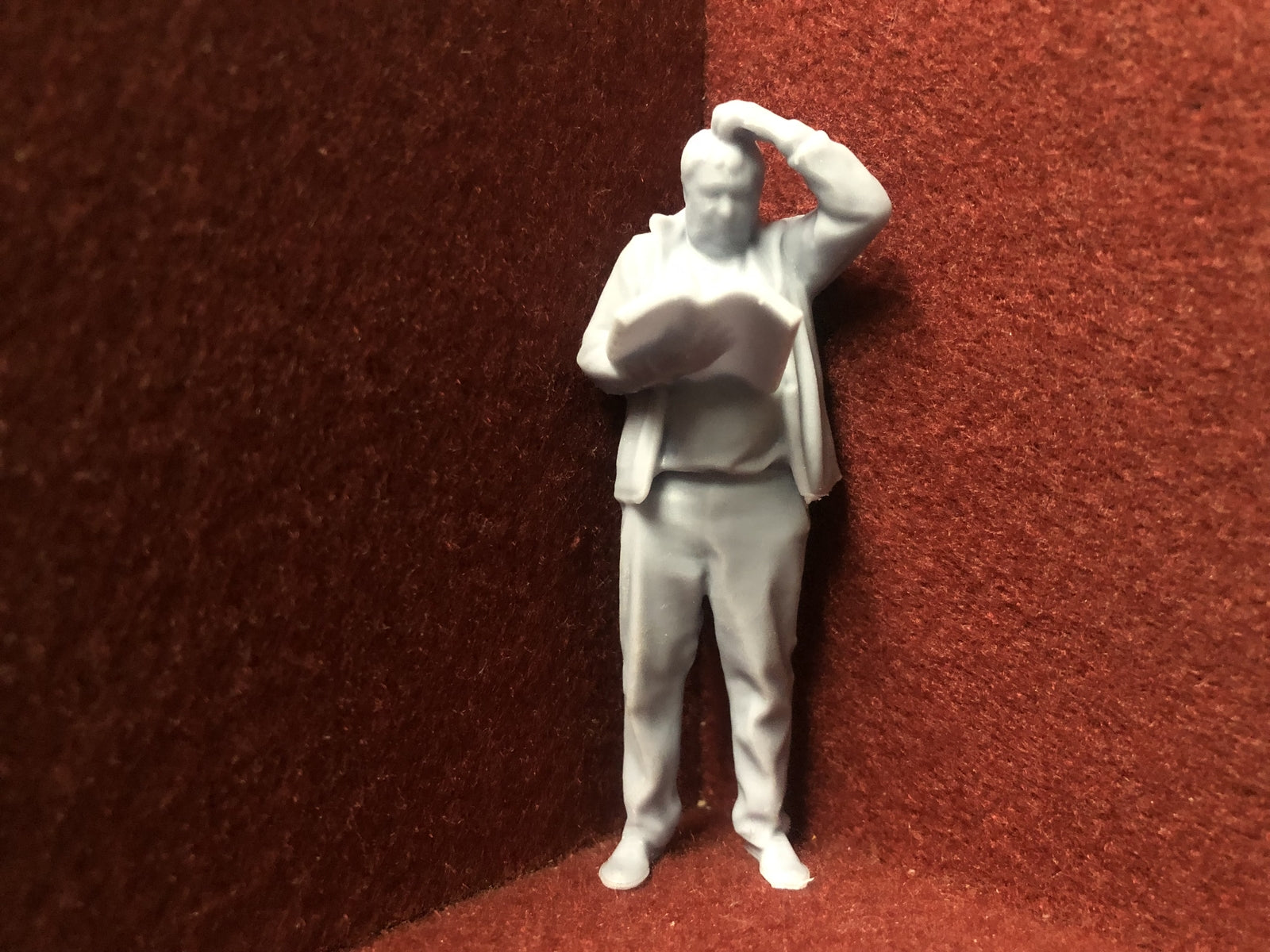 Unpainted G-scale 1:22.5 driver figure for model railways, 3D scanned from a real person, holding a manual and looking perplexed.