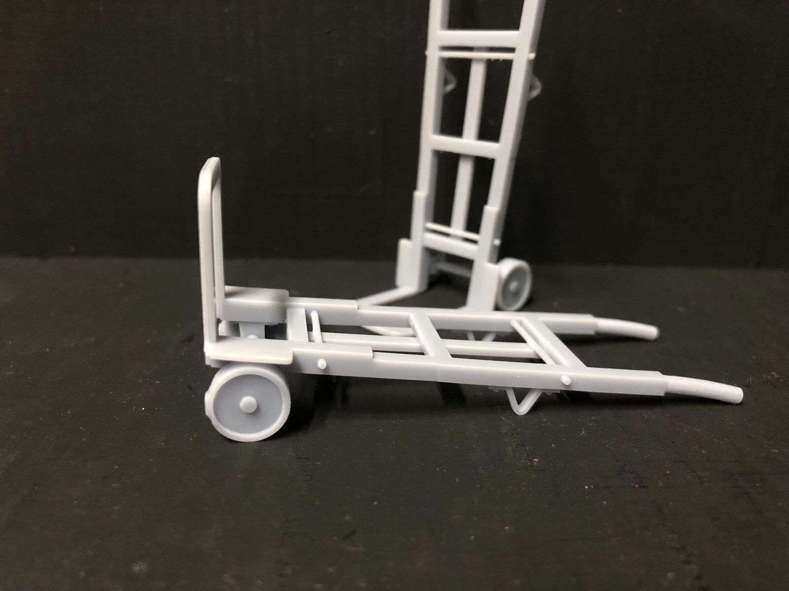 Unpainted 16mm scale resin pair of sack trolleys for model railway platforms or workshop scenes, shown in grey ready for painting