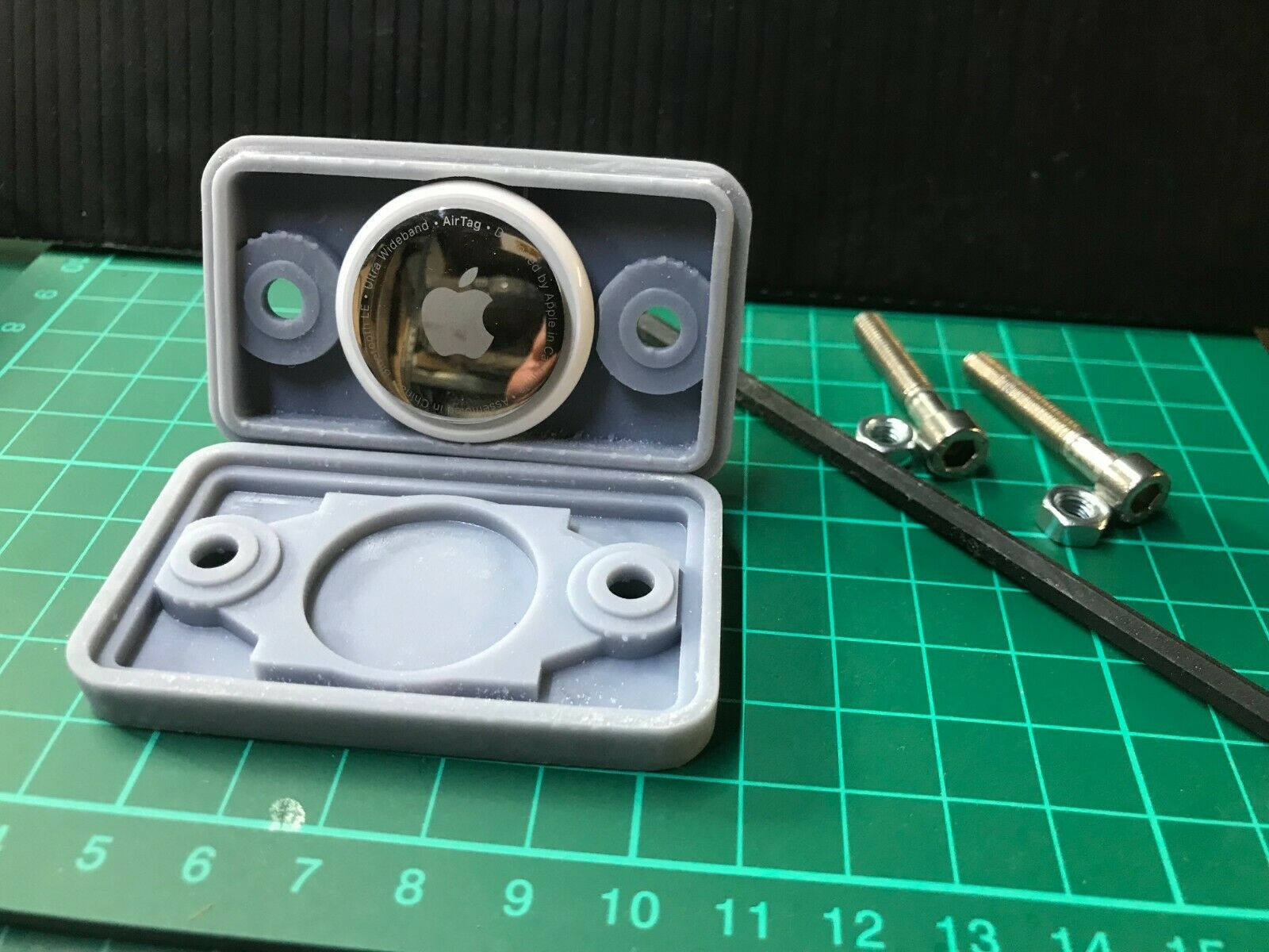 Black stealth covert case for an Apple AirTag, shown open to reveal the hidden compartment for tracking a car or motorbike